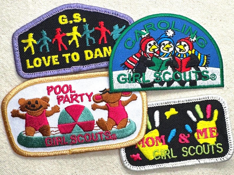 May include: A collection of Girl Scout patches with various designs. One patch features dancing figures, another shows penguins reading, and a third depicts bears at a pool party. Other patches include the phrases "Mom & Me" and "Love to Dan".