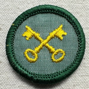 May include: Embroidered patch featuring two crossed yellow keys on a light green background. The patch has a dark green border with detailed stitching. The design is circular and appears to be a badge or emblem.