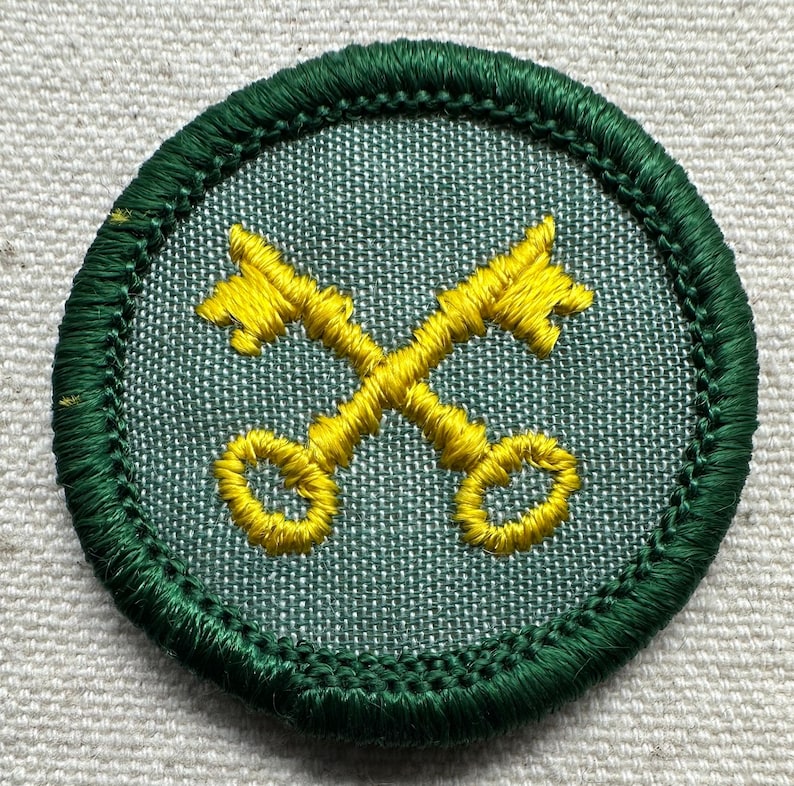 May include: Embroidered patch featuring two crossed yellow keys on a light green background. The patch has a dark green border with detailed stitching. The design is circular and appears to be a badge or emblem.