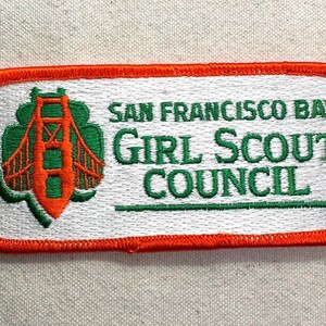May include: Embroidered patch featuring the words "SAN FRANCISCO BAY GIRL SCOUT COUNCIL" in green text. The patch has a white background with an orange border. A green and orange image of the Golden Gate Bridge is on the left.