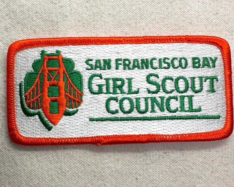 May include: Embroidered patch featuring the words "SAN FRANCISCO BAY GIRL SCOUT COUNCIL" in green text. The patch has a white background with an orange border. A green and orange image of the Golden Gate Bridge is on the left.
