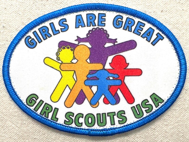 May include: Oval patch with a blue border featuring the text "GIRLS ARE GREAT" and "GIRL SCOUTS USA." The patch has a white background with colourful figures in yellow, orange, purple, red, and blue.