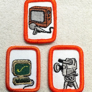 May include: Three embroidered patches with orange borders. One patch features a brown television with a microphone. Another shows a computer with a green screen. The third depicts a vintage movie camera.