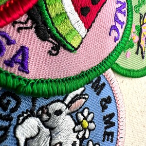 May include: Close-up of embroidered patches with various designs. One patch features a watermelon slice, another a rabbit with daisies, and others with text. The patches have a variety of colors, including pink, green, blue, and white.