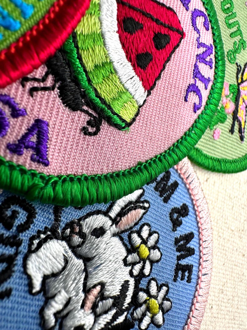 May include: Close-up of embroidered patches with various designs. One patch features a watermelon slice, another a rabbit with daisies, and others with text. The patches have a variety of colors, including pink, green, blue, and white.