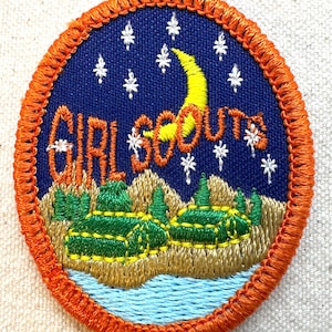 K&ouml;nnte beinhalten: Gestickter Girl Scouts-Aufn&auml;her mit orangefarbenem Rand. Der Aufn&auml;her zeigt einen blauen Nachthimmel mit wei&szlig;en Sternen und einem gelben Halbmond. Die Worte "GIRL SCOUTS" sind wei&szlig; gestickt. Darunter eine Landschaft mit gr&uuml;nen B&auml;umen und einem blauen Fluss.