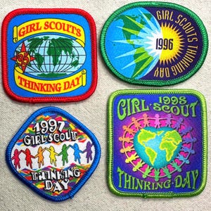 May include: Four Girl Scout Thinking Day patches. The patches are square and circular, with various designs including globes, the years 1995, 1996, 1997, and 1998, and the words "Girl Scouts Thinking Day."