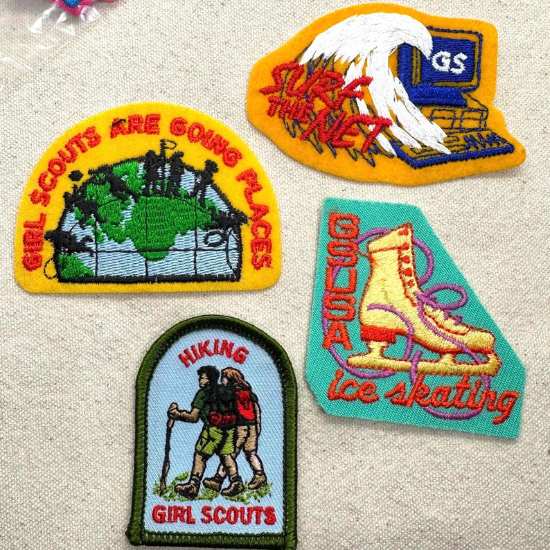 May include: A collection of embroidered Girl Scout patches. Designs include a world map with text "Girl Scouts Are Going Places", a wave with text "Surf the Net", an ice skate with text "Ice Skating", and two hikers with text "Hiking".