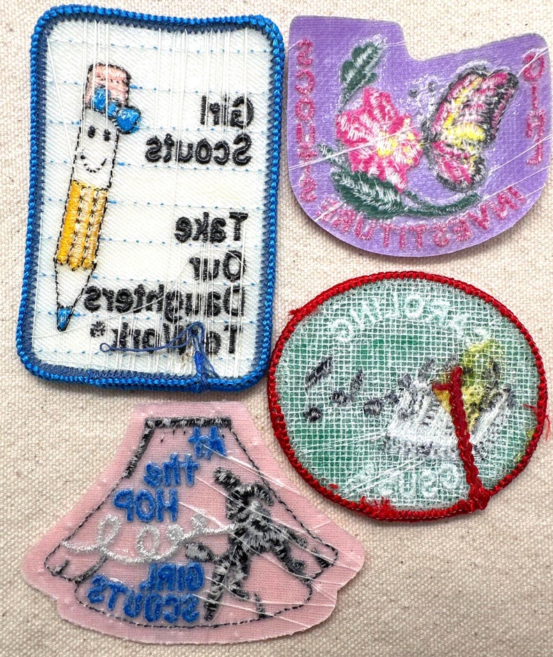 May include: Four Girl Scout patches with various designs. One patch features a smiling pencil with the text "Girl Scouts Take Our Daughters To The Top". Another shows a butterfly and flowers. A third patch has a girl dancing. The last patch has a bird.