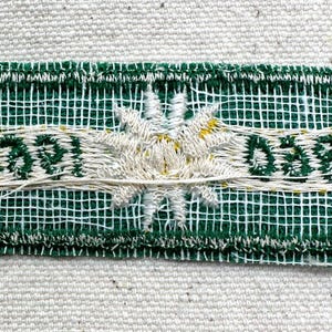 May include: Embroidered patch with a green mesh background and white stitching. The patch features a central white flower design and the text "0591" and "0581" in white. Yellow accents are visible.