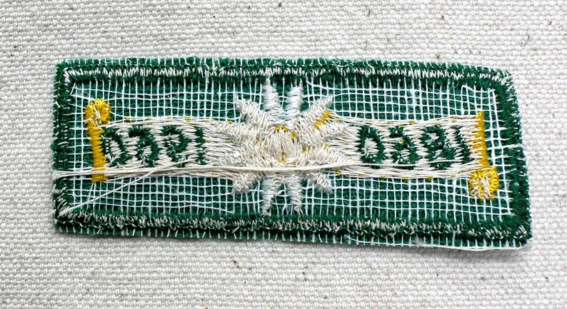 May include: Embroidered patch with a green mesh background and white stitching. The patch features a central white flower design and the text "0591" and "0581" in white. Yellow accents are visible.