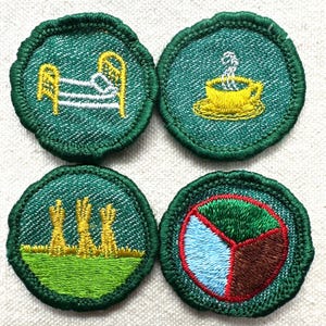 May include: Four green embroidered patches with various designs. One patch features a bed, another a teacup, a third depicts wheat, and the last has a segmented design in green, blue, and brown. Each patch has a green border.