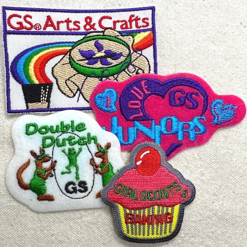Puede incluir: Cuatro parches bordados con texto y gr&aacute;ficos. Un parche dice "GS Arts & Crafts" con un dise&ntilde;o de arco&iacute;ris y mano. Otros parches incluyen "Double Dutch", un coraz&oacute;n con "Love Juniors" y una magdalena que dice "Girl Scouts Baking".