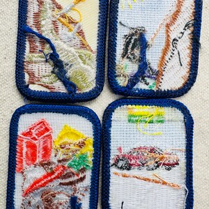 May include: Four embroidered patches with blue borders. The patches feature various outdoor scenes, including mountains, a person climbing, and a vehicle. The patches are rectangular with a white background and colorful thread details.