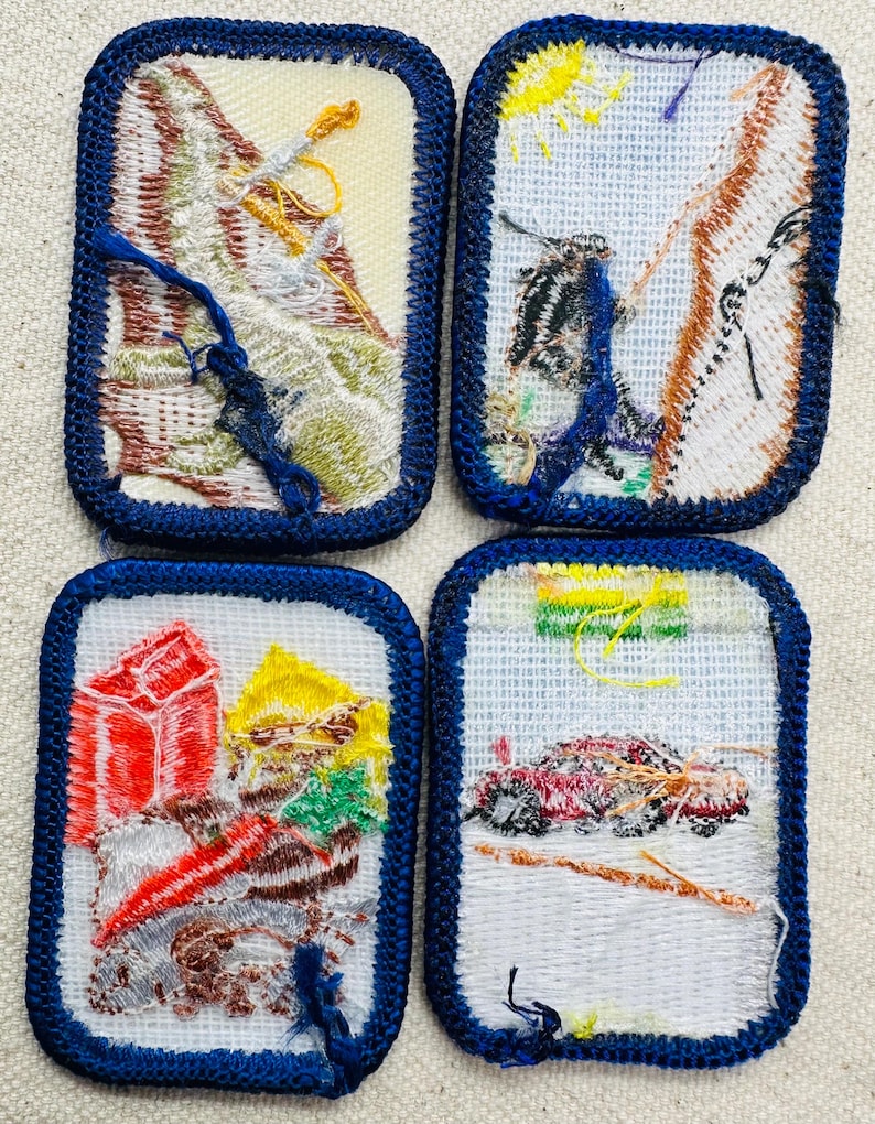 May include: Four embroidered patches with blue borders. The patches feature various outdoor scenes, including mountains, a person climbing, and a vehicle. The patches are rectangular with a white background and colorful thread details.