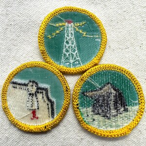 May include: Three vintage round patches with yellow embroidered borders. Each patch features a different design: a radio tower, a person with a flag, and a small shelter. The patches have a green and white color scheme.