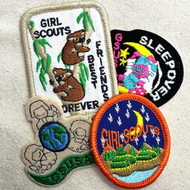 K&ouml;nnte beinhalten: Eine Sammlung von Girl Scout-Abzeichen. Ein Abzeichen zeigt Koalas und den Text "Girl Scouts Forever Friends". Ein weiteres Abzeichen hat einen Halbmond und Sterne mit den Worten "Girl Scouts". Ein drittes Abzeichen sagt "Sleepover".