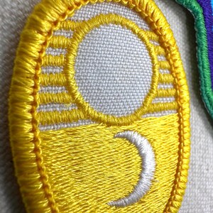 Puede incluir: Parche amarillo bordado con un dise&ntilde;o de luna creciente blanca y sol. El parche tiene un borde amarillo y est&aacute; sobre una tela gris claro. El dise&ntilde;o es un tema celestial estilizado.