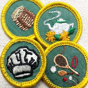 May include: Four embroidered patches with green backgrounds and yellow borders. The patches feature images of a loaf of bread, a teapot with flowers, a chef's hat, and cooking utensils. The patches are likely for a youth organization.