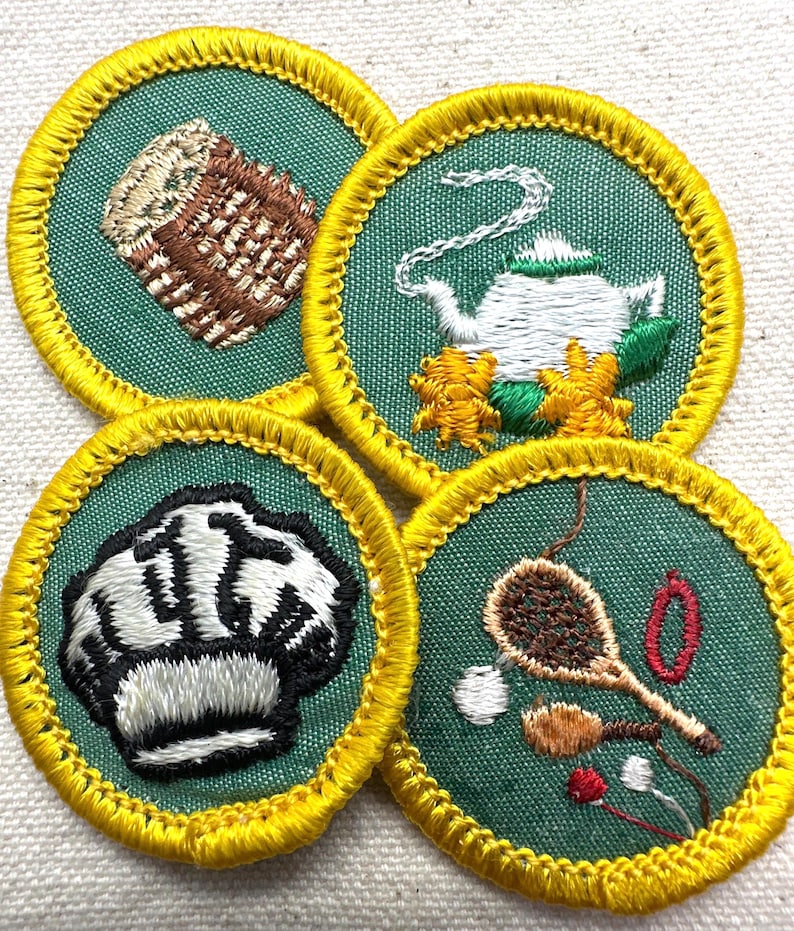 May include: Four embroidered patches with green backgrounds and yellow borders. The patches feature images of a loaf of bread, a teapot with flowers, a chef's hat, and cooking utensils. The patches are likely for a youth organization.