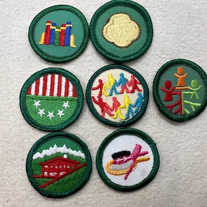May include: A collection of embroidered patches with green borders. The patches feature various designs, including a building, a clover, and figures holding hands. The patches are likely for a youth organization.