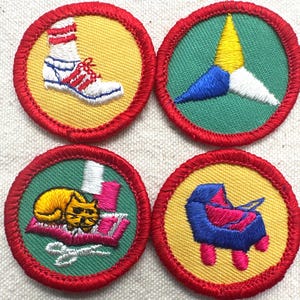 May include: Four embroidered patches with red borders. One features a white sneaker with red stripes and a white sock on a yellow background. Another shows a multi-colored starburst on green. A third depicts a cat on a book. The last shows a blue and pink object.