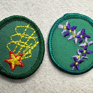 May include: Two embroidered patches. One is green with a yellow and red starburst design. The other is green with a floral pattern of purple and yellow flowers. Both patches have a green border.