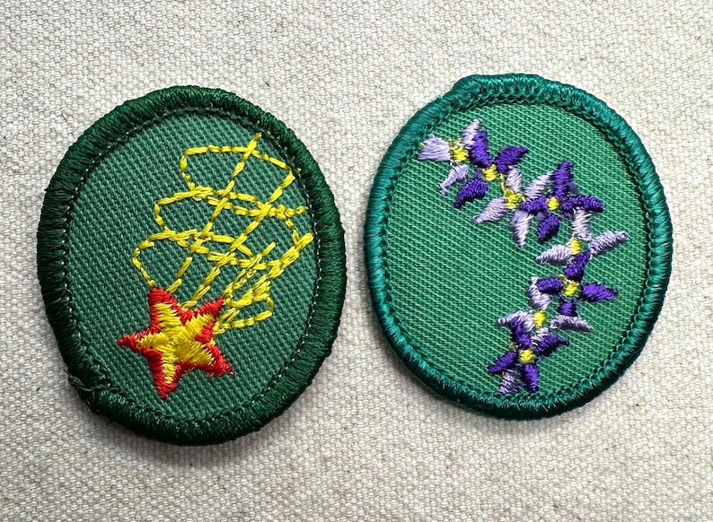 May include: Two embroidered patches. One is green with a yellow and red starburst design. The other is green with a floral pattern of purple and yellow flowers. Both patches have a green border.