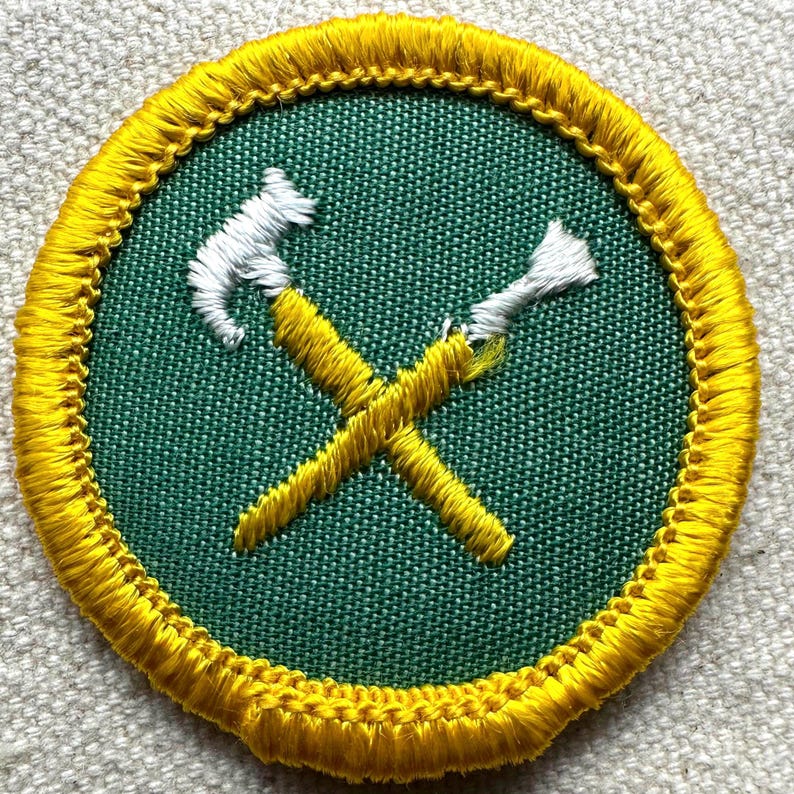 Pode incluir: Patch bordado com um centro verde com ferramentas amarelas cruzadas e cabe&ccedil;as de ferramentas brancas. O patch &eacute; circular com uma borda amarela.