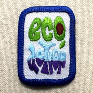 May include: Embroidered patch with a white background and a blue border. The patch features the word "eco" in green, an avocado, and the words "better" and "swim" in blue and purple. The patch is rectangular with rounded corners.