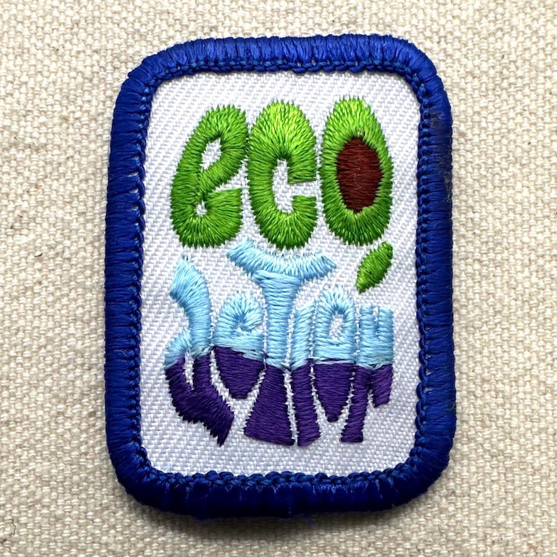 May include: Embroidered patch with a white background and a blue border. The patch features the word "eco" in green, an avocado, and the words "better" and "swim" in blue and purple. The patch is rectangular with rounded corners.