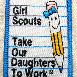 May include: Embroidered Girl Scouts patch with a blue border. The patch features the text "Girl Scouts Take Our Daughters To Work" in black, along with a smiling pencil illustration with a pink eraser and blue bow.