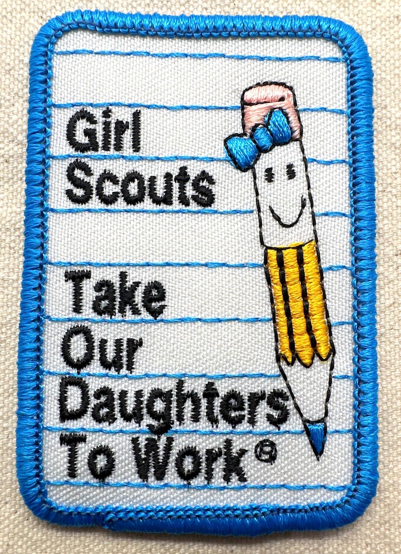 May include: Embroidered Girl Scouts patch with a blue border. The patch features the text "Girl Scouts Take Our Daughters To Work" in black, along with a smiling pencil illustration with a pink eraser and blue bow.