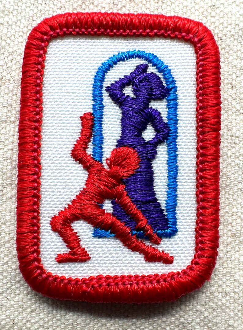 Puede incluir: Parche bordado con borde rojo y centro blanco. El dise&ntilde;o presenta dos figuras estilizadas: una figura roja en movimiento y una figura morada dentro de un arco azul. El parche es probablemente para ropa o accesorios.