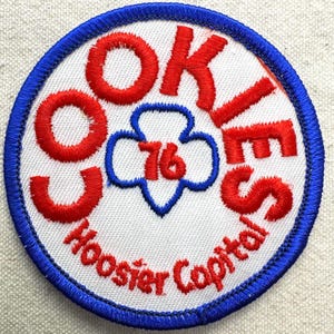 May include: Embroidered patch with a white center, featuring the words "COOKIES" in red, and "Hoosier Capital" in red at the bottom. A blue trefoil with the number "76" in red is in the center. The patch has a blue border.