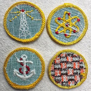 May include: Four circular embroidered patches with yellow edging. Designs include a lighthouse, an atom, an anchor, and a plaid pattern. The patches are stitched on a light blue mesh background.