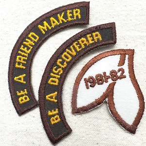 May include: Three embroidered patches. Two are brown with yellow text that reads "BE A FRIEND MAKER" and "BE A DISCOVERER". The third patch is white with brown trim and the text "1981-82".