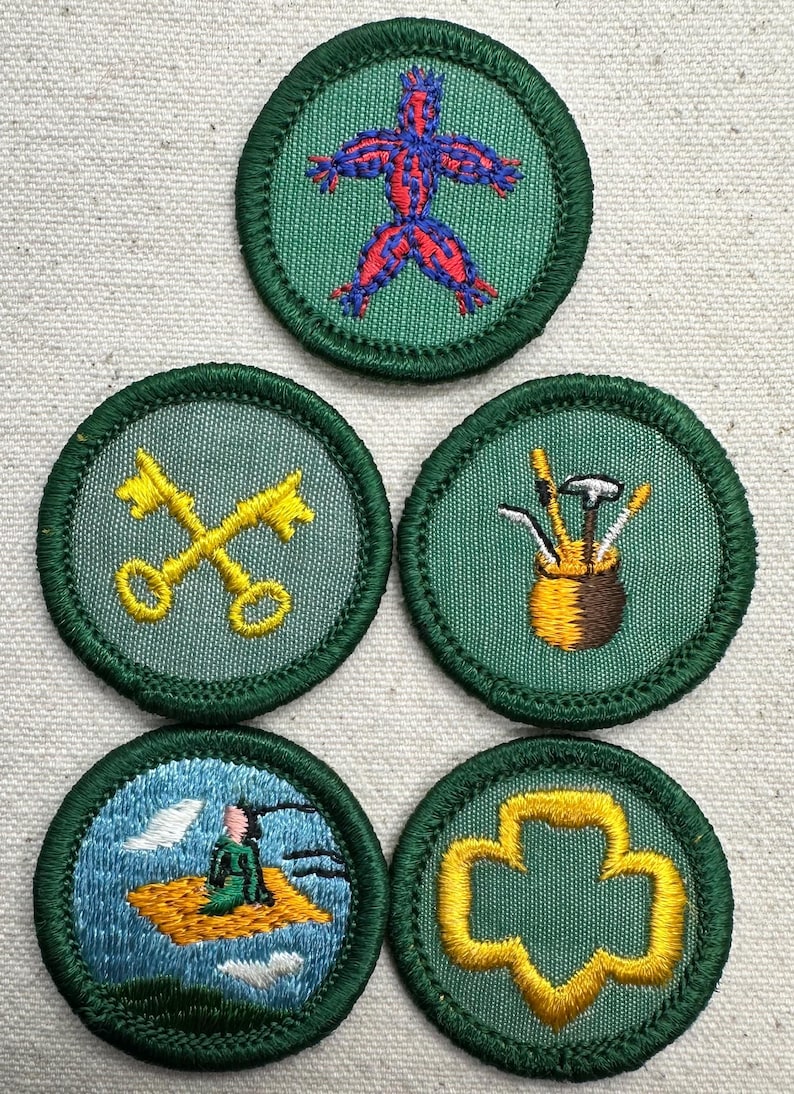 May include: Five embroidered patches with green borders. Designs include a figure, crossed keys, golf clubs in a bag, a person on a flying carpet, and a trefoil. The patches are circular and have a green background.