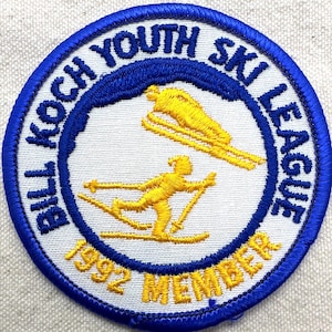 May include: Embroidered patch with a blue border and the text "Bill Koch Youth Ski League." The patch features yellow skiers on a white background, with "1992 MEMBER" in yellow text. A circular design, suitable for apparel or collectibles.