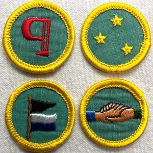 May include: Four embroidered patches with a green background and yellow border. The patches feature a red letter "q", three yellow stars, a flag with black, white, and blue sections, and two hands shaking. These patches are likely for a club or organization.