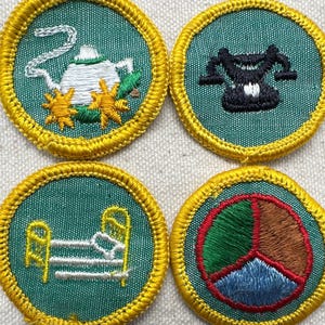 May include: Four embroidered patches with a teal background and gold trim. The patches feature a teapot, a scale, a bed, and a peace sign. The patches are likely for a youth organization or similar.