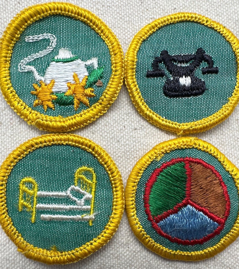 May include: Four embroidered patches with a teal background and gold trim. The patches feature a teapot, a scale, a bed, and a peace sign. The patches are likely for a youth organization or similar.