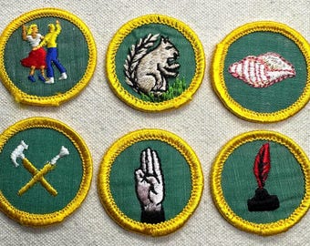 Puede incluir: Seis parches bordados con bordes amarillos y centros verdes. Los parches presentan varios diseños, incluyendo una pareja bailando, una ardilla, una concha, herramientas cruzadas, un gesto con la mano y una pluma.