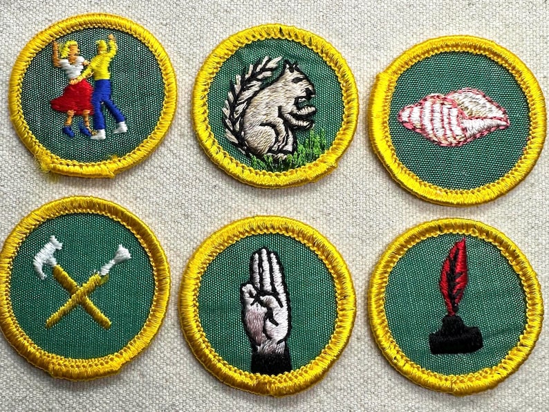 Pode incluir: Seis patches bordados com bordas amarelas e centros verdes. Os patches apresentam v&aacute;rios designs, incluindo um casal dan&ccedil;ando, um esquilo, uma concha, ferramentas cruzadas, um gesto de m&atilde;o e uma pena.