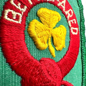 May include: Embroidered patch featuring the text "BE PREPARED" in white on a red ring, encircling a yellow shamrock on a green backdrop. The patch, with a green border, is likely for a scouting uniform or similar organisation.