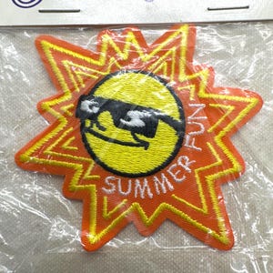 May include: Embroidered patch featuring a yellow sun wearing sunglasses, set against an orange starburst design. The words "SUMMER FUN" are embroidered in white. The patch is packaged in clear plastic.