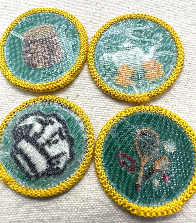 May include: Four round patches with green centers and yellow embroidered borders. The patches feature various designs, including a basket, flowers, a baseball, and a spoon with flowers. The patches are likely for a youth organization.