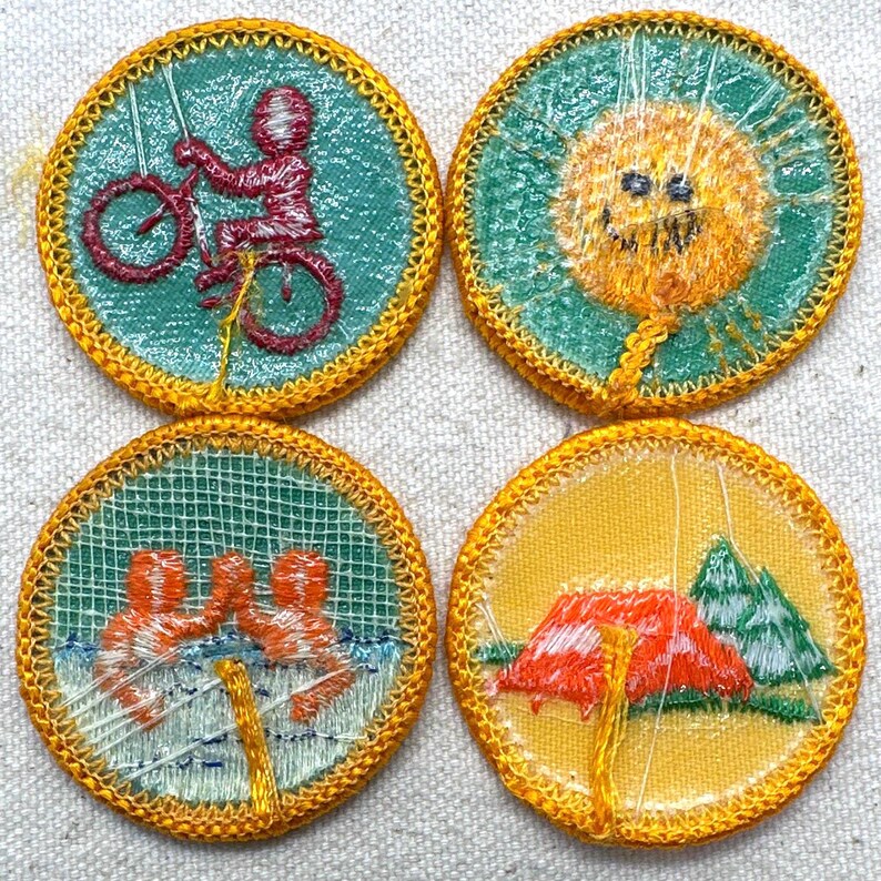 Puede incluir: Cuatro parches bordados circulares con bordes amarillos. Uno muestra a una persona en bicicleta, otro un sol sonriente, un tercero representa a personas nadando y el &uacute;ltimo presenta una tienda de campa&ntilde;a y &aacute;rboles. Cada parche tiene un fondo de color diferente.