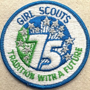 May include: Embroidered Girl Scouts patch with a blue border. The patch features the words "Girl Scouts" and "Tradition with a Future." The number "75" is prominently displayed, surrounded by stars.