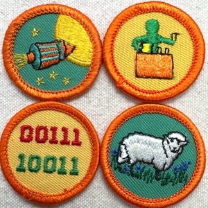 May include: Four round embroidered patches with orange borders. Designs include a rocket, a person on a box, binary code, and a sheep. The patches have green and yellow backgrounds with detailed stitching.